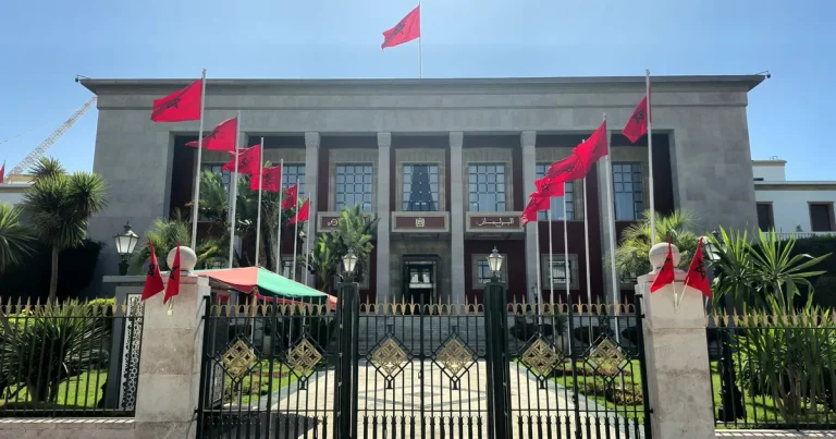 Fachada del Parlamento de Marruecos en Rabat, engalanada con banderas marroquíes bajo un cielo azul